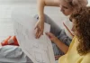 Czy warto inwestować w nieruchomości w dużym mieście? Dwie młode kobiety siedzą na podłodze i oglądają rzut mieszkania.