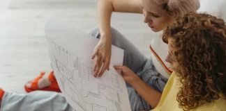 Dwie młode kobiety siedzą na podłodze i oglądają rzut mieszkania.