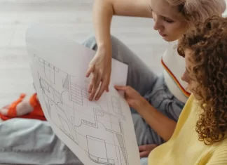 Czy warto inwestować w nieruchomości w dużym mieście? Dwie młode kobiety siedzą na podłodze i oglądają rzut mieszkania.